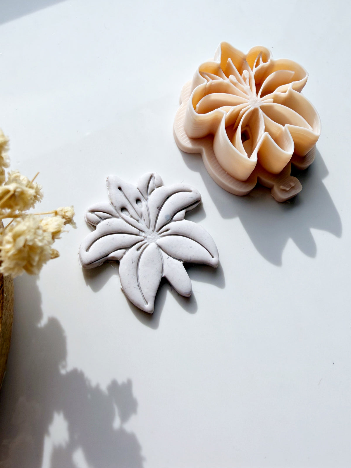 Flower-shaped polymer clay cutter next to a pressed clay impression on a white surface.