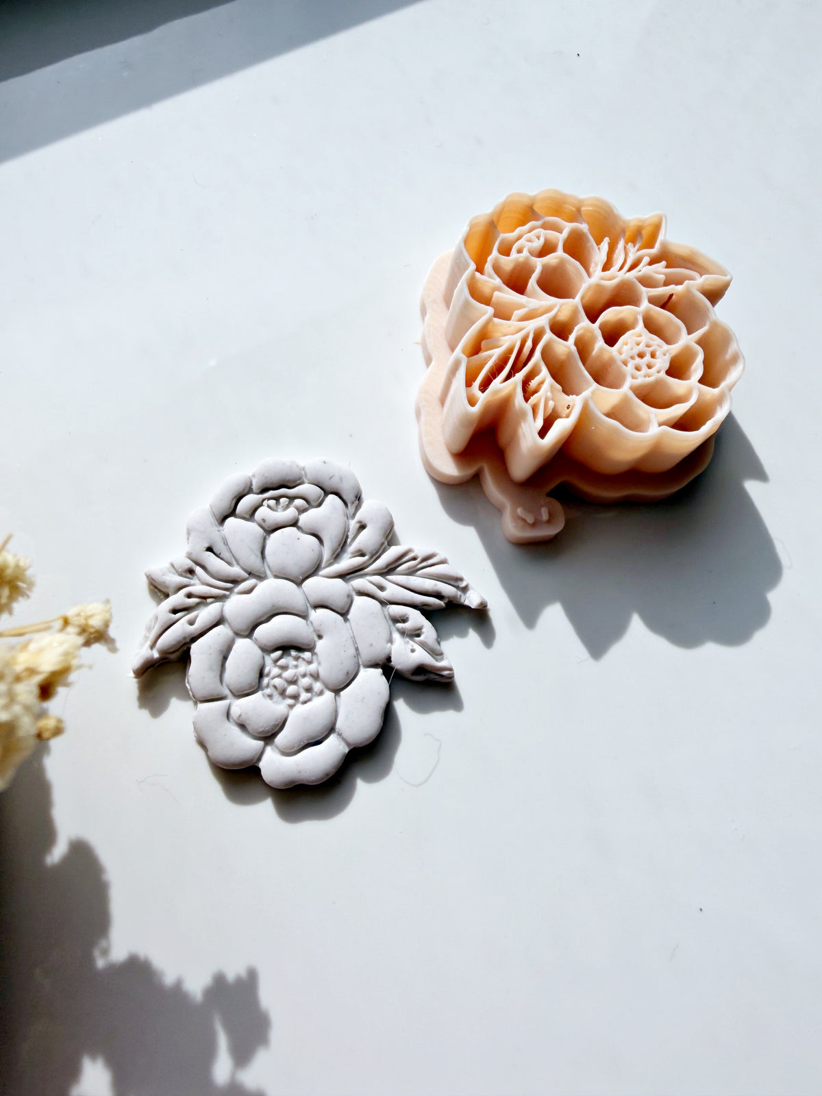 Peach floral cookie cutter next to a grey embossed fondant flower design on a white surface.