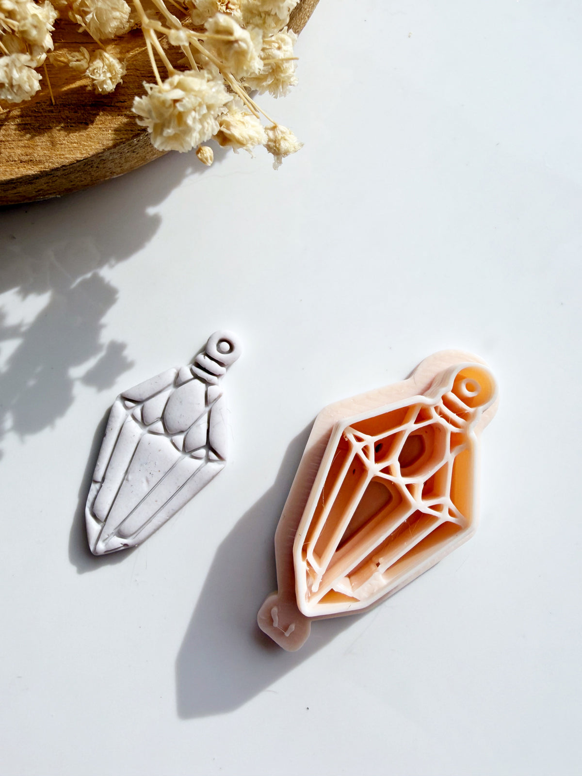 Geometric diamond crystal pendant clay cutter with a matching white polymer clay shape on a white background.