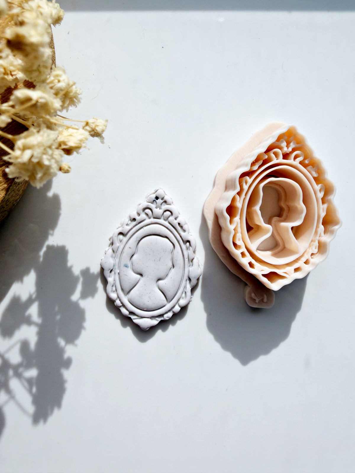 Victorian cameo portrait polymer clay cutter and embossed clay charm on a white background with decorative dried flowers.